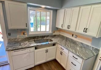 remodeled kitchen with white cabinets, black hardware, and gray countertops
