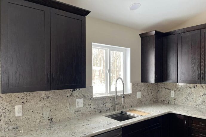 remodeled kitchen with black cabinets and gray countertops/stone backsplash